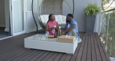 Afro-Amerikalı çift modern terasta hediye kutlaması ve içeceklerin tadını çıkarıyorlar. Kutlama, yıldönümü, modern, açık hava, eğlence, çift, rahatlama, ortam