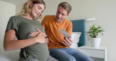 Beklenen çift evde neşeyle kaynaşıyor, hamile karnına sevgiyle dokunuyor. Hamilelik, aile, beklenti, ebeveynlik, annelik, mutluluk