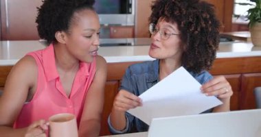 Evde dizüstü bilgisayar kullanarak kahkahalarla gülen ve kahvenin tadını çıkaran farklı kadın çiftleri severdik. İlişki, teknoloji, eğlence, mutluluk