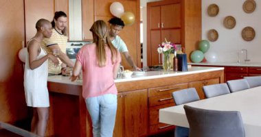 Partide, arkadaşlar mutfakta toplanır, yemek ve içecekleri yemek masasına taşır, gülümserler. Arkadaşlık, kutlama, akşam yemeği, gündelik, yaşam tarzı, birliktelik