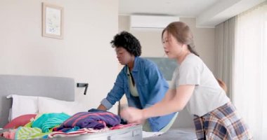 Afro-Amerikalı ve Asyalı arkadaşlar bavulları ve kıyafetleriyle kızlar için yatak odasına toplanıyorlar. Paketleme, kaçış, arkadaşlık, stil, organizasyon, modern macera, eğlence