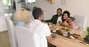 Çeşitli arkadaşlar evde öğle yemeğinin tadını çıkarıyor, kahkahalar ve sohbetler ediyorlar. Arkadaşlık, yemek, toplanma, sosyalleşme, yaşam tarzı, mutluluk.