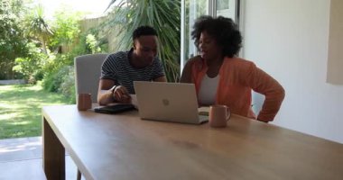 Afro-Amerikalı çift evde laptopları ve tabletleriyle iş konuşuyorlar. Uzak çalışma, takım çalışması, işbirliği, dijital aygıtlar, iletişim, teknoloji