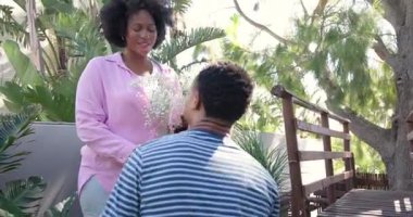 Genç çift bahçede romantik anlar yaşıyor, ellerinde çiçekler ve neşeyle gülümsüyorlar. Romantizm, aşk, mutluluk, doğa, ilişki