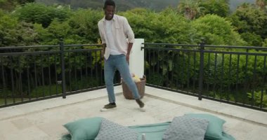 Afro-Amerikalı bir adam verandaya giriyor, battaniye, yastıklar, şarap şişesiyle tepsi yerleştiriyor. Rahatlama, açık havada yaşam, rahatlık, zarif, rahat, rahat giysi, kırsal