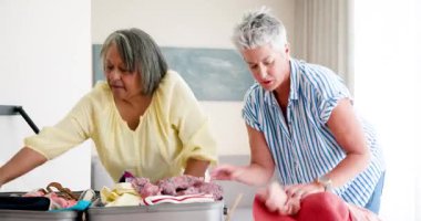 Üst düzey arkadaşlar kapalı mekanı dekore ediyor, kutlama malzemeleriyle gri bavulu düzenliyorlar. Kutlama, dostluk, işbirliği, ev, dekor, yaşlılar, neşeli, rahat