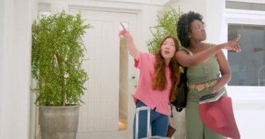 Afro-Amerikalı, Asyalı arkadaşlar kırmızı çanta ve bavullarıyla parlak girişe geliyorlar. Seyahat, buluşma, macera, arkadaşlık, giriş, bagaj, tatil, doğal ışık