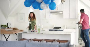 Peçete alıyor, kıdemli çift tost için mutfak adasında balonların altına şarap bardakları koyuyor. Kutlama, mahremiyet, zarafet, boş zaman, sade, romantik, keyifli