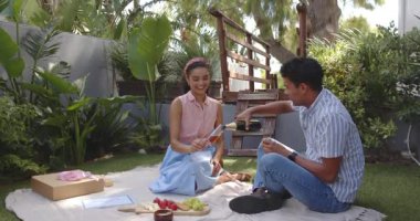 Çeşitli çiftler bahçede yıldönümlerini kutluyor. Meyve ve ve şampanyayla piknik battaniyesinin keyfini çıkarıyorlar. Kutlama, piknik, romantizm, açık hava, neşe, birliktelik, yeşillik, mutluluk