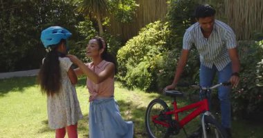 Bahçede kırmızı bisiklete binen çeşitli aile rehberi kız, mavi kasklı. Öğrenme, bisiklet, açık hava, destek, aile, macera, büyüme, doğa