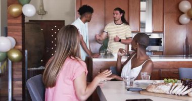 Arkadaşların evde eğleniyor, yemek ve içeceklerle sofra kuruyor, gülümsüyor. Kutlama, toplanma, arkadaşlık, yemek, ev, misafirperverlik.