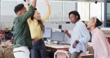 Afro-Amerikan takımı pozitif haberler veren tablet ekranı izliyor ve ofis masalarında kutluyor. İşbirliği, takım çalışması, yenilik, başarı, coşku, çeşitlilik, modernizasyon