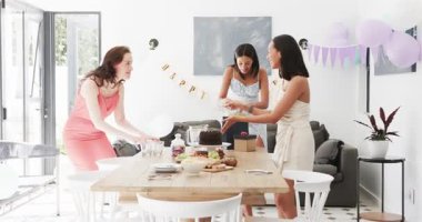 Çeşitli bayan arkadaşlar pasta, balon, doğum günü afişi astıktan sonra yemek masasında hediye düzenliyorlar. Kutlama, dostluk, yaşam tarzı, modern, mutlu, toplanma, renkli