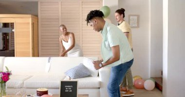 Çizgili gömlekli bir adam oturma odasında balonlarla yürüyor, düşünceli görünüyor. Düşünce, ev içi, kutlama, yalnızlık, gündelik, düşünceli