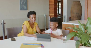 Anne oğluna ödevlerinde yardım ediyor, tablet kullanıyor ve notlar yazıyor. Ebeveynlik, aile, teknoloji, eğitim, öğrenim, bağlanma