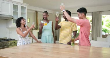 Çeşitli arkadaşlar gülüyor ve içkilerini parlak mutfakta, ahşap adada içiyorlar. Mutfak, toplantı, arkadaşlık, kutlama, misafirperverlik, kahkaha, modern