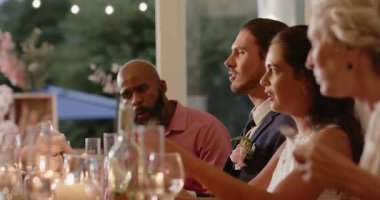 Çeşitli düğün masası grupları kamera dışı konuşmaya tepki veriyor damat kadeh kaldırıyor, gelin gülümsüyor. Kutlama, yoldaşlık, zarafet, neşe, şenlik, birliktelik, sıcaklık.