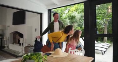 Eve gelen, çantalarını taşıyan, şapka takan, yemek masasına güneş gözlüğü takan farklı bir aile. Aile, eve dönüş, modern iç mekan, yaşam tarzı, neşeli, açık hava, rahat