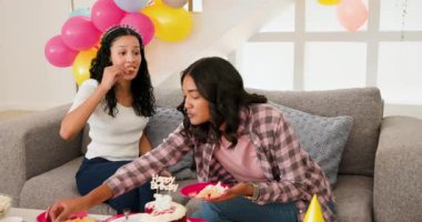 Oturma odasındaki gri kanepede oturan çeşitli bayan arkadaşlar, kek aperatifleriyle pembe tabakları paylaşıyorlar. Doğum günü, kutlama, balonlar, pastel, hediyeler, gündelik konuşma