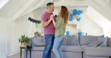 Üst düzey çift, partneri dans ederken, doğum günü afişi altında kutlama yaparken fark ediyor. Romantik, kutlama, samimiyet, neşe, arkadaşlık, kapalı mekanlar, samimi