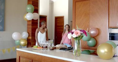 Partide, arkadaşlar evde kutlama yapıyor, sohbet ediyor ve mutfak adasında atıştırmalıkların tadını çıkarıyor. Arkadaşlık, kutlama, parti, toplanma, sosyalleşme, rahatlama.