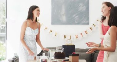 Üç bayan arkadaş evde pasta düzenliyor ve kutlama için hediye paketi hazırlıyorlar. Kutlama, dostluk, mutluluk, neşe, dekor, samimi, neşeli