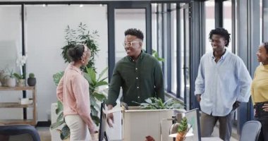 Modern ofiste yeni iş arkadaşını kutlayan Afro-Amerikalı iş arkadaşları, bitki kutuları, ofis eşyaları. İşbirliği, takım çalışması, takım oluşturma, gemiye binme, selamlama, sürpriz, alkış