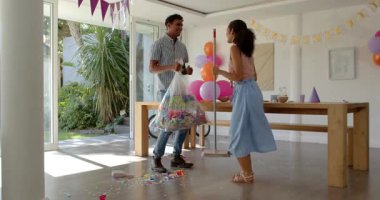 Çeşitli çiftler konfeti temizliyor ve ellerinde renkli balonlarla evde parti masası hazırlıyorlar. Kutlama, şenlik, renkli, toplanma, neşe, temizlik, dekorasyon, parti