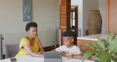 Anne oğluna ödevlerinde yardım ediyor evde tablet kullanıyor, ikisi de konsantre oluyor. Ebeveynlik, aile, dijital öğrenme, eğitim, teknoloji, öğretim