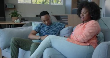 Afro-Amerikalı çift evde dinleniyor, kadın kanepede oturuyor, adam mutfakta. Yaşam tarzı, eğlence, aile içi, ilişki, birliktelik, rahatlama.