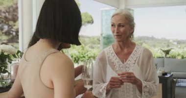 Tavsiyeden sonra, müstakbel gelini ve arkadaşları balkonda şampanya kadehleri kaldıran kıdemli anne. Kutlama, arkadaşlık, zarafet, neşe, açık hava, lüks, neşe