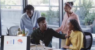 Modern ofisteki bilgisayar monitöründe, saksı bitkisi olan Afrikalı Amerikalı iş arkadaşları grafikleri analiz ediyorlar. Profesyoneller, takım çalışması, işbirliği, beyin fırtınası, analitik, yenilik, çağdaş