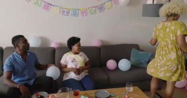 Çeşitli arkadaşlar evde kutlama yapıyor, kadın hediye paketini heyecan ve neşeyle açıyor. Kutlama, arkadaşlık, hediye verme, mutluluk, parti, sürpriz