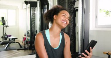 Spor kıyafetleriyle gülümseyen kadın spor salonunda akıllı telefonu kontrol ediyor. Fitness, egzersiz, teknoloji, yaşam tarzı, sağlık, sağlık