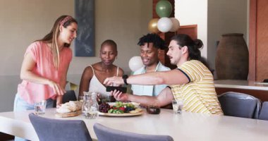 Partide arkadaşlar güler ve yemek masasında abur cubur ve içeceklerle akıllı telefonu paylaşırlar. Arkadaşlık, sosyalleşme, eğlence, teknoloji, toplama, eğlence.