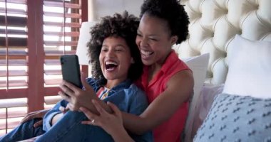 Evde, rahat yatak odası ortamında akıllı telefondan video sohbeti yaparken çeşitli kadın çiftler gülüyor. kahkaha, video çağrısı, mutluluk, eğlence, teknoloji