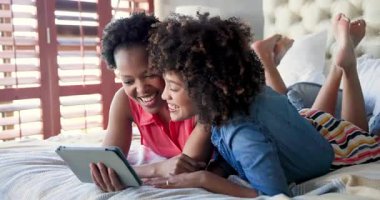 İki kadın yatakta dinleniyor, gülümsüyor ve evde tablet kullanıyor. Teknoloji, rahatlama, arkadaşlık, eğlence, mutluluk, iletişim