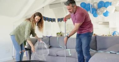 Doğum günü partisinden sonra, yaşlı çift oturma odasını süpürüyor, çöp torbasında flamalar topluyorlar. Kutlama, takım çalışması, ev işi, temizlik, gündelik, neşeli, uyum