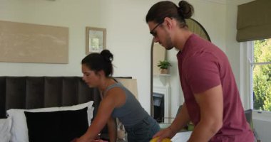 Yatak odasında bavulları boşaltan, elbiselerini düzenleyen, güneş gözlüğü takan ve hasır şapka takan çift. Romantizm, seyahat, macera, yaşam tarzı, organizasyon, paketleme, eğlence