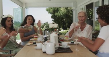 Verandadaki çeşitli bayan arkadaşlar pasta paylaşıyorlar ve şampanya içen gelinler kahkahalar atıyorlar. Kutlama, dostluk, zarafet, açık hava, rahatlık, dostluk, sofistike