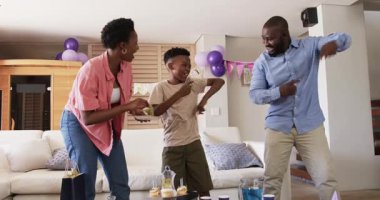 Aile evde kutlama yapıyor, balonlar ve abur cuburlarla neşeyle dans ediyor. Kutlama, mutluluk, parti, şenlik, eğlence, birliktelik