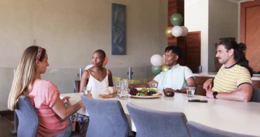 Partide, arkadaşlar yemek masasında yemek ve içeceklerle sohbet edip kahkaha atıyorlar. Arkadaşlık, toplanma, kutlama, yemek, sosyalleşme, mutfak.