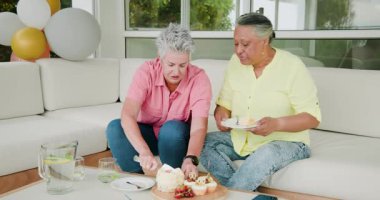 60. doğum gününü oturma odasında kutlayan kıdemli arkadaşlar pasta dilimleri, pasta ve içki paylaşıyorlar. Kutlama, arkadaşlar, sevinç, toplanma, pasta, konfor, doğum günü