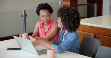 Evde dizüstü bilgisayar kullanırken gülümseyen ve sarılan Afrikalı lezbiyen çift. Çeşitlilik, teknoloji, arkadaşlık, bağlanma, mutluluk, yaşam tarzı
