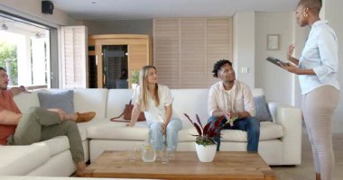 Tabletli Afro-Amerikalı kadın evdeki kanepede arkadaşlarıyla tartışıyor. Sosyalleşme, teknoloji, arkadaşlık, rahatlama, çeşitlilik, yaşam tarzı