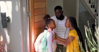 Afro-Amerikalı aileler, kızın nane pembesi çantasını ayarlıyor ve kapıyı açmadan önce sarılıyorlar. Aile bağları, çocukluk anları, banliyö evi, ev hayatı, duygusal bağlantı, yaşam tarzı, sıcak atmosfer