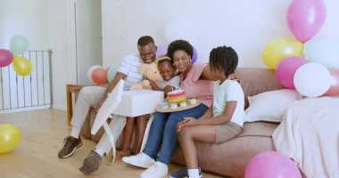 Afrikalı Amerikalı bir aile doğum gününü kanepesinde pasta ve balonlarla kutluyor. Kutlama, aile, mutluluk, konfor, birliktelik, coşku, balonlar