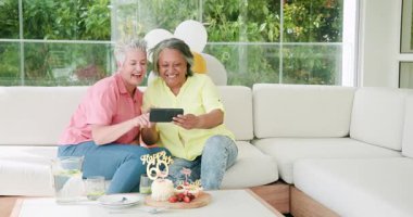 60. yaş gününü içeride kutlayan kıdemli arkadaşlar, ahşap masadaki doğum günü pastasına içki döküyorlar. Kutlama, arkadaşlar, doğum günü, sevinç, toplanma, pasta, coşku