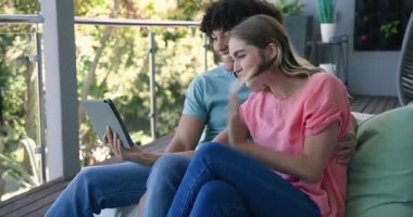 Genç çift tablette görüntülü sohbet ediyor, balkonda oturuyor, gülümsüyor ve el sallıyor, evde. Teknoloji, iletişim, dijital, yaşam tarzı, birliktelik, eğlence