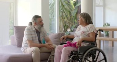 Evlat, yaşlı anneyi tekerlekli sandalyeyle oturma odasına itiyor terlikleri çıkarıyor, pencere kenarına ayakkabıları monte ediyor. Bakım, aile, destek, arkadaşlık, ev, sıcaklık, şefkat.